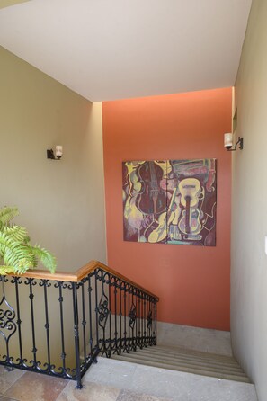 A staircase with a railing, a wall-mounted light fixture, and a painting of musical instruments. - XTILU Hotel - Adults only (Oaxaca)