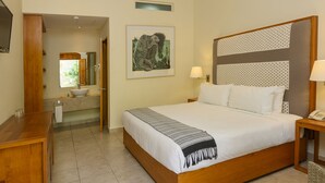 A hotel room with a large bed, a wooden desk, a bathroom with a sink and mirror, and a framed picture on the wall. - XTILU Hotel - Adults only (Oaxaca)