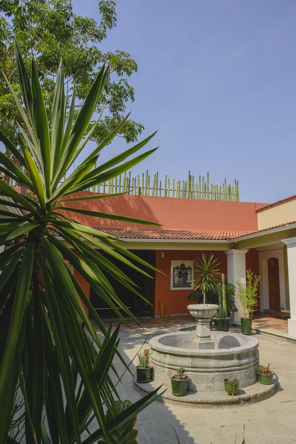 A courtyard with a fountain, potted plants, and a building with a red roof. - XTILU Hotel - Adults only (Oaxaca)