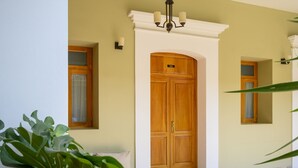 A wooden double door with a number plate, a white wall, and a small window with a curtain. - XTILU Hotel - Adults only (Oaxaca)