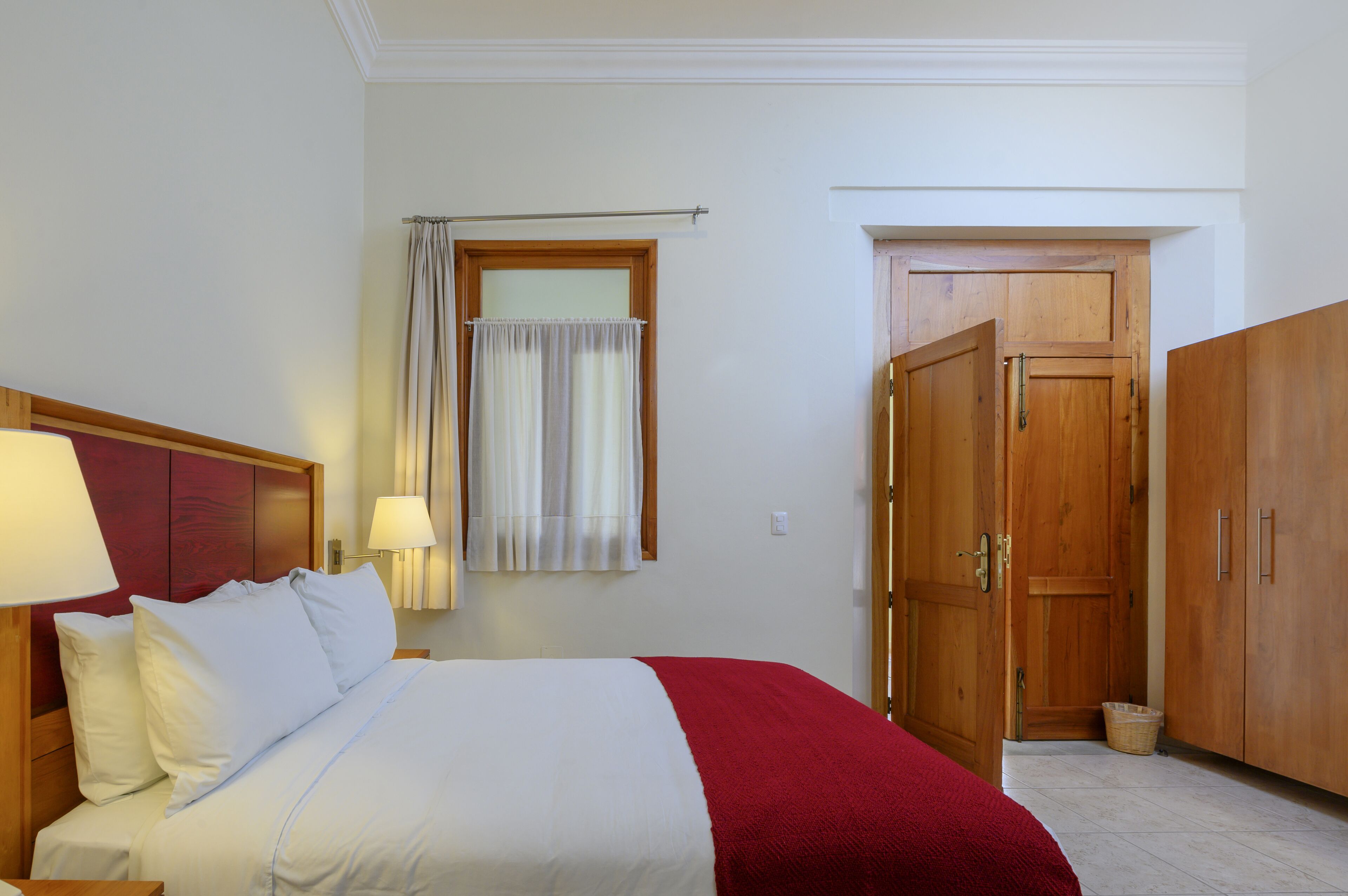 Ein Hotelzimmer mit einem Bett, einem Nachttisch, einer Lampe, einem Fenster mit Vorhängen und Holzschränken.