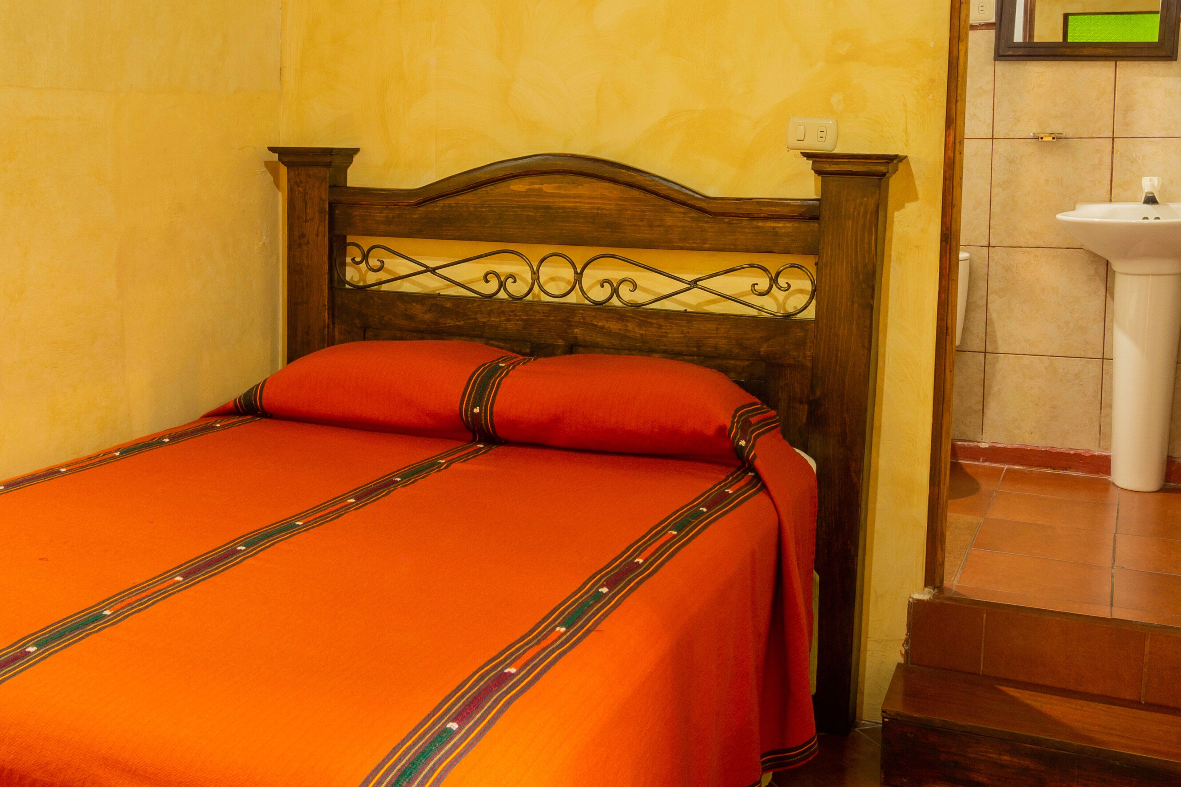 Cama bem arrumada com cabeceira de madeira e colcha vermelha.