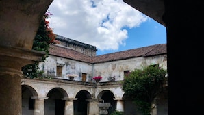 An open courtyard with a fountain, arches, and a building with a tiled roof. - Hotel Maya Ik (Antigua Guatemala)