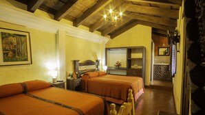 A hotel room with two beds, wooden headboards, a chandelier, a painting, and a bathroom visible in the background. - Hotel Maya Ik (Antigua Guatemala)