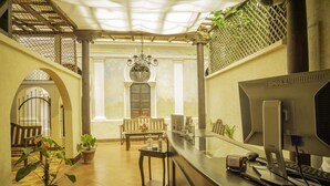A reception area with a desk, computer, and potted plants. There is a bench and a window in the background. - Hotel Maya Ik (Antigua Guatemala)