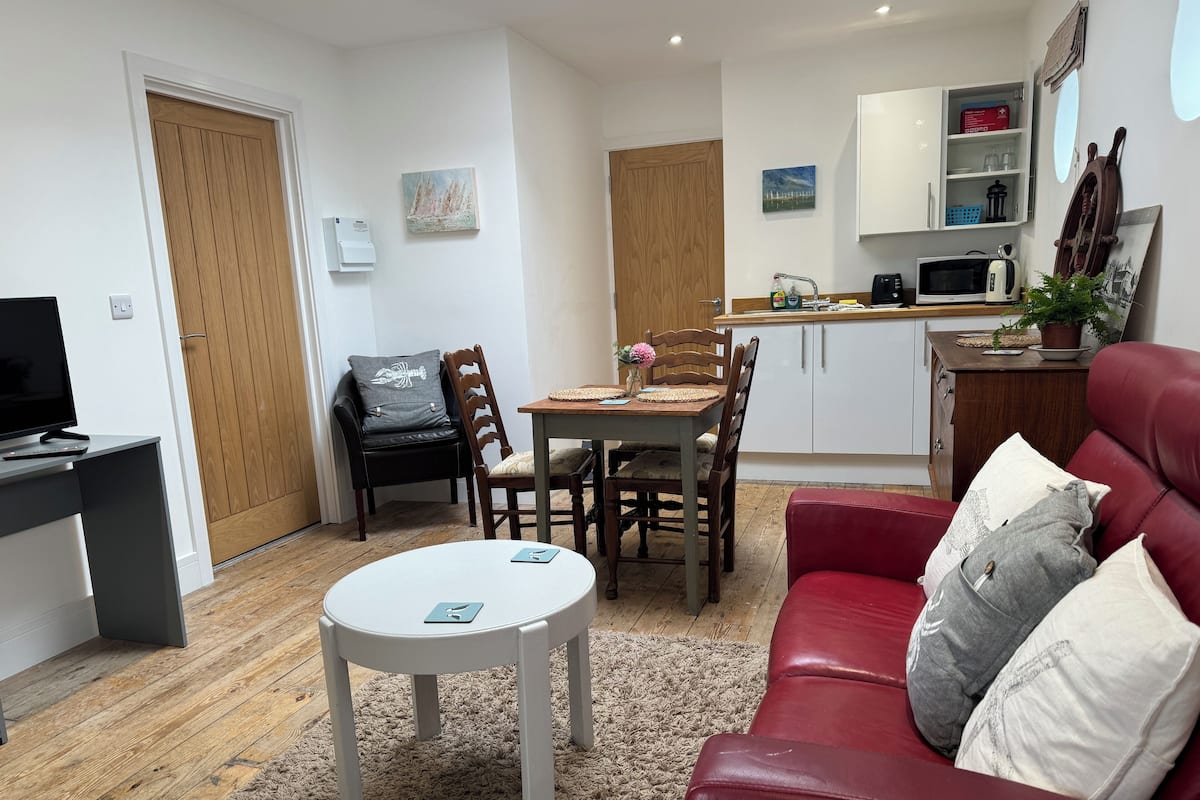Un espacio habitable compacto con comedor, kitchenette y un sofá rojo.