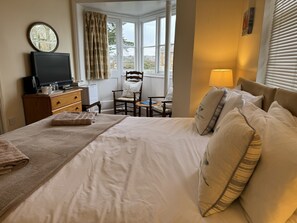 A neatly made bed with pillows and a blanket, a television on a dresser, a chair, and a window with curtains. - The Pilot Boat Inn (Bembridge)