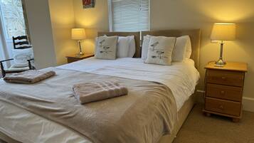 A neatly made bed with a beige blanket and pillows, two bedside lamps, a wooden nightstand, and a chair with a cushion.