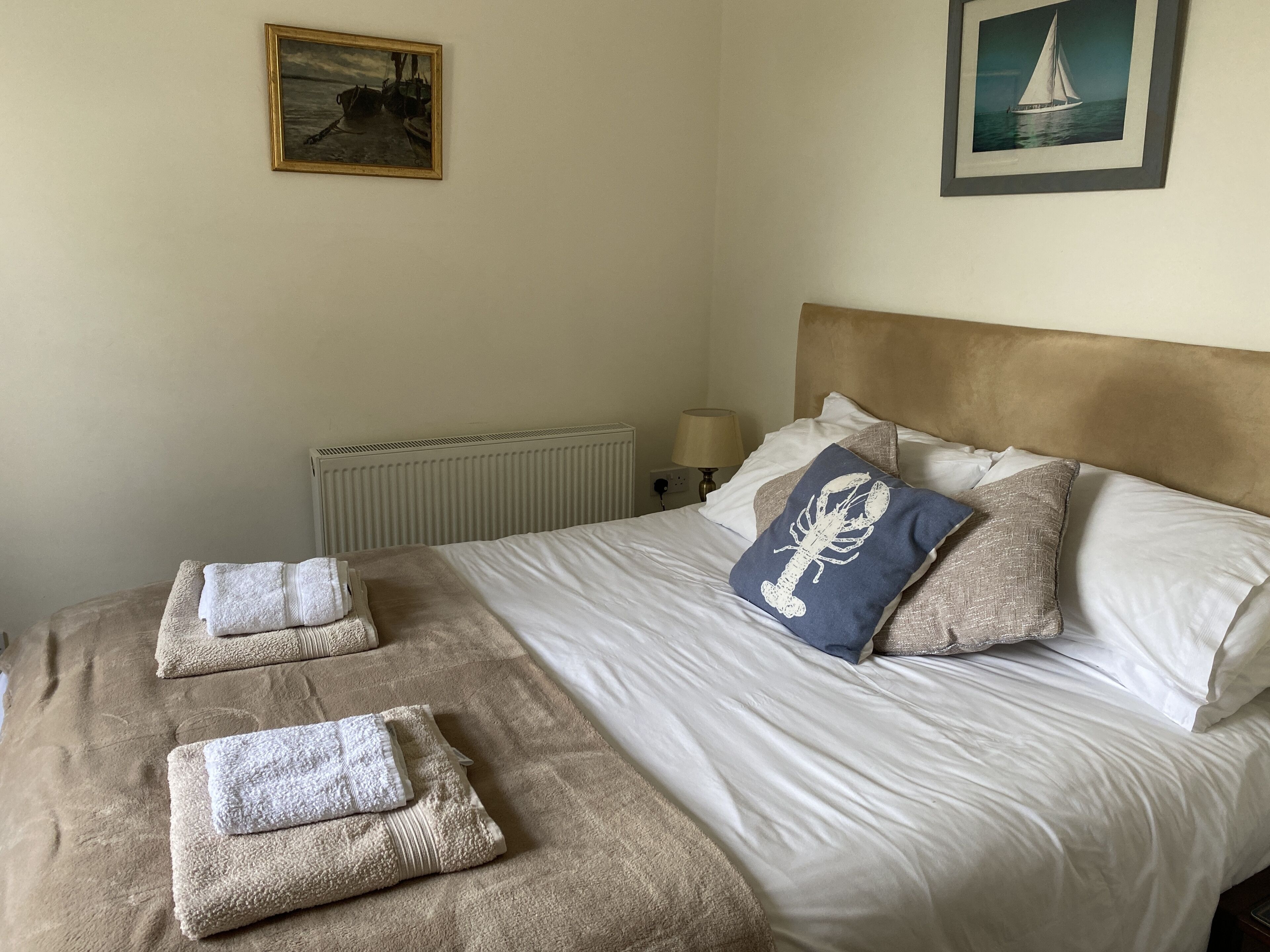 A neatly made bed with white linens, a blue pillow with a scorpion design, and two folded towels on the bed.