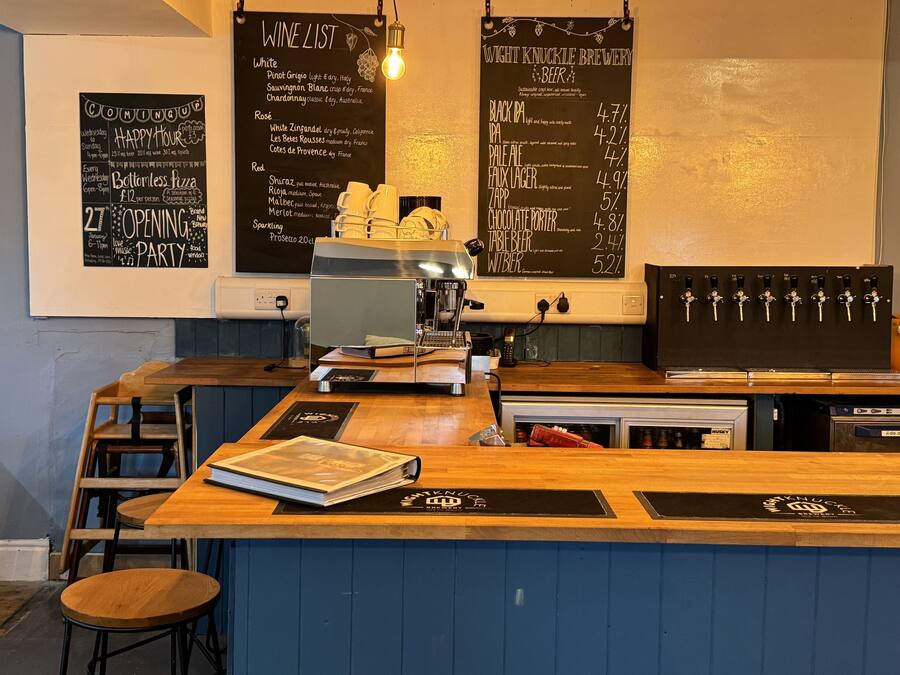 Zona de bar con un menú en la pizarra que enumera varios vinos y cervezas, una máquina de café y una barra de madera.