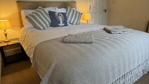 Una cama bien hecha con almohadas a rayas, una manta estampada y una toalla doblada.