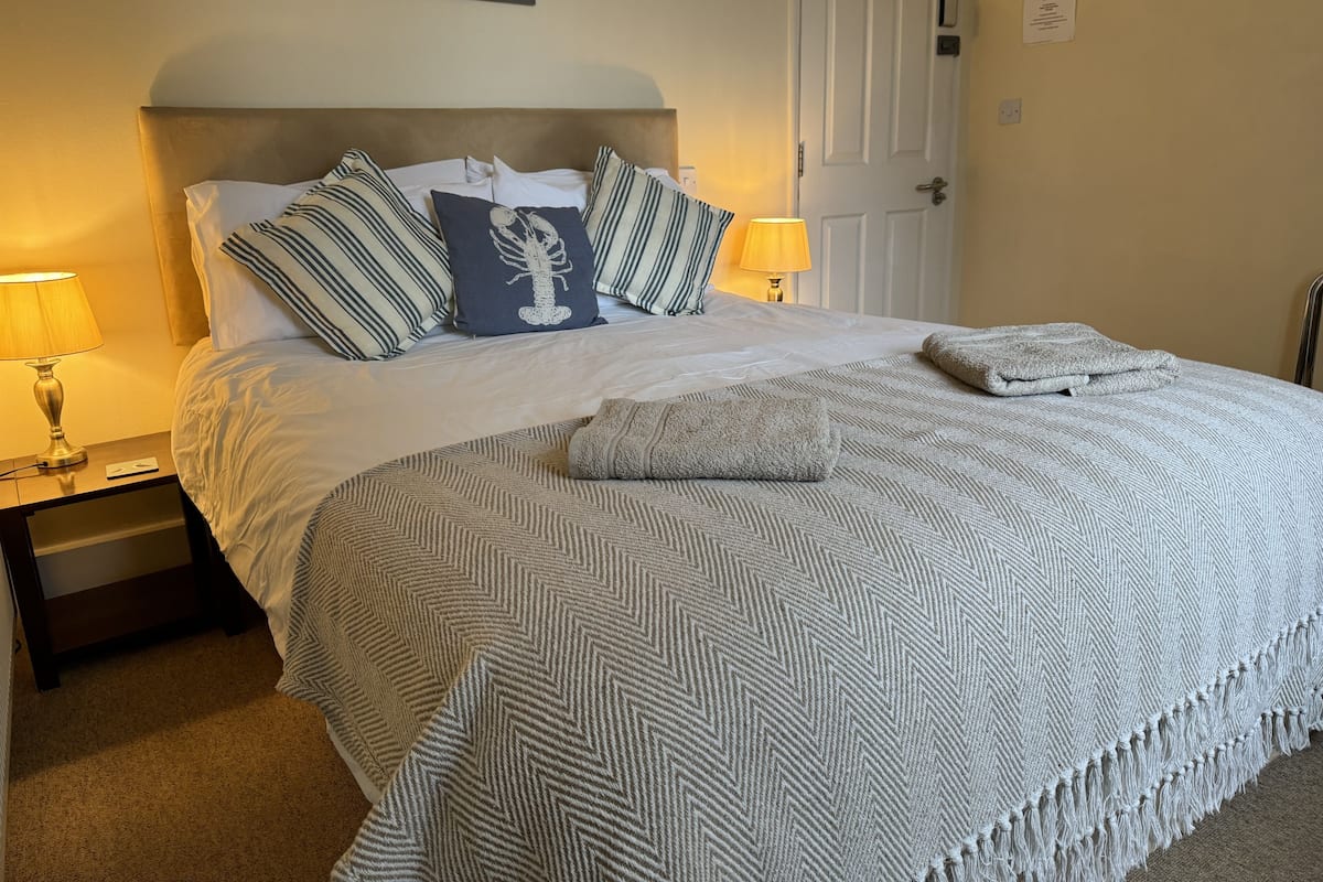 Una cama bien hecha con almohadas a rayas, una manta estampada y una toalla doblada.