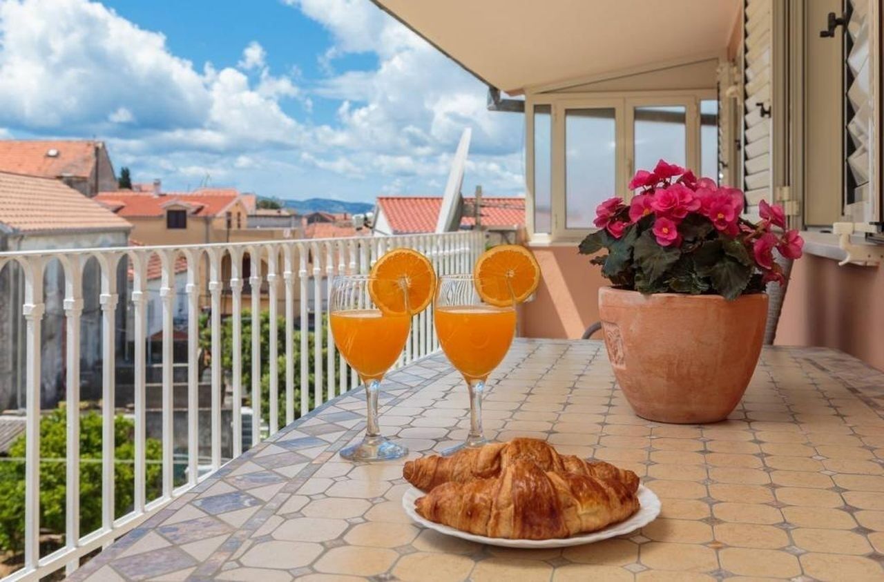 A balcony with a table set for breakfast, including croissants and orange juice, overlooking a cityscape.