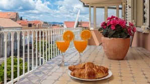 A balcony with a table set for breakfast, including croissants and orange juice, overlooking a cityscape.