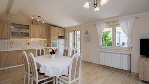 A kitchen with wooden cabinets, a white table with chairs, a vase with flowers, and a window with curtains.