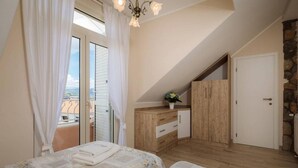 A bedroom with two beds, a wooden dresser, a stone wall, and a balcony with curtains.