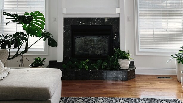 A living room with a fireplace, white walls, and large windows with blinds.