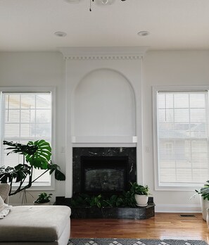A living room with a fireplace, white walls, and large windows with blinds. - 3 Bedroom Spacious Residential Home (Sedalia)