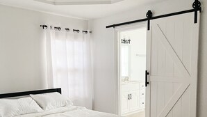 A bedroom with a bed, a ceiling fan, a white door, and a view to the outside.