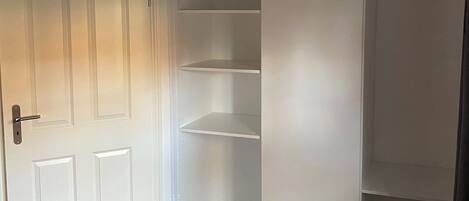 Una habitación con una puerta blanca, una cama con colcha a rayas y una estantería empotrada blanca con varios compartimentos.
