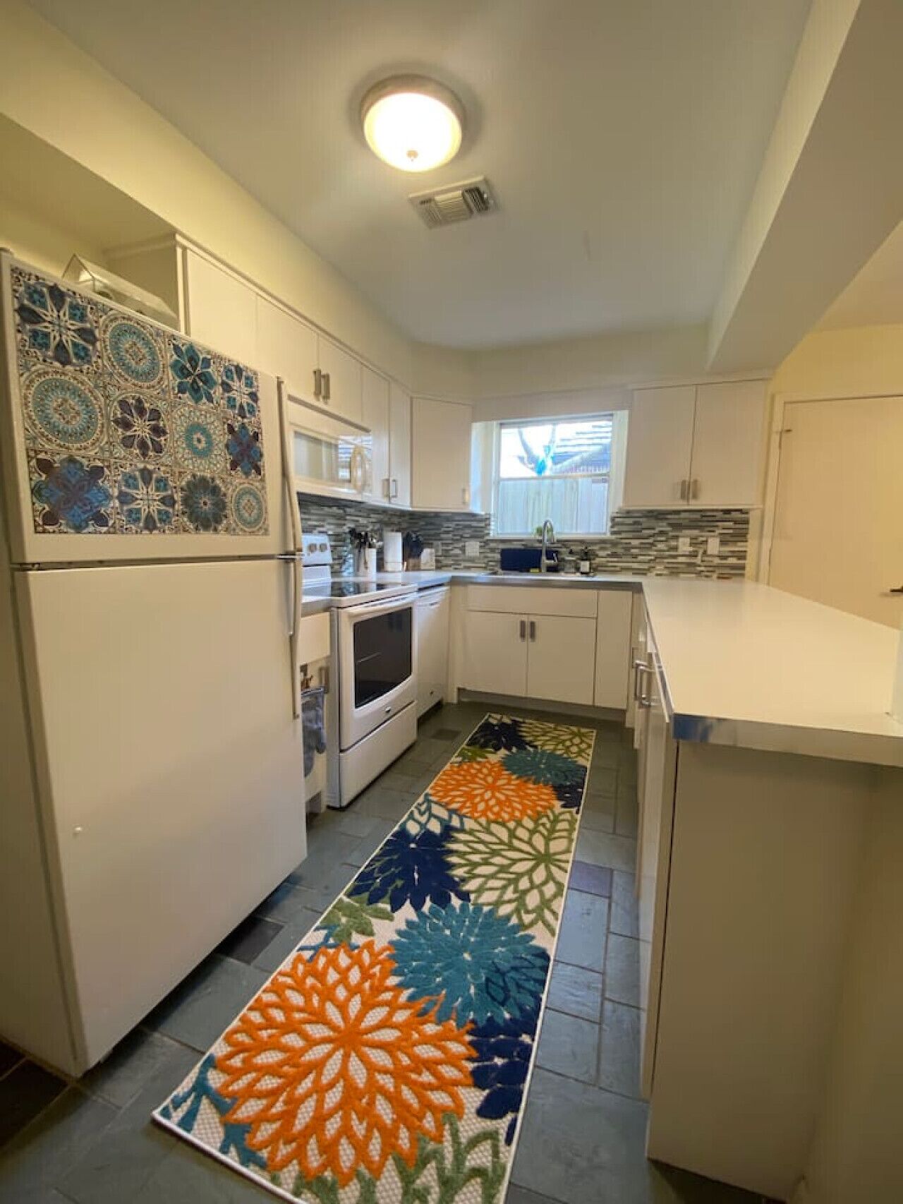 Une cuisine avec des meubles blancs, un pare-feu en carreaux, un tapis à motifs et un four encastré.