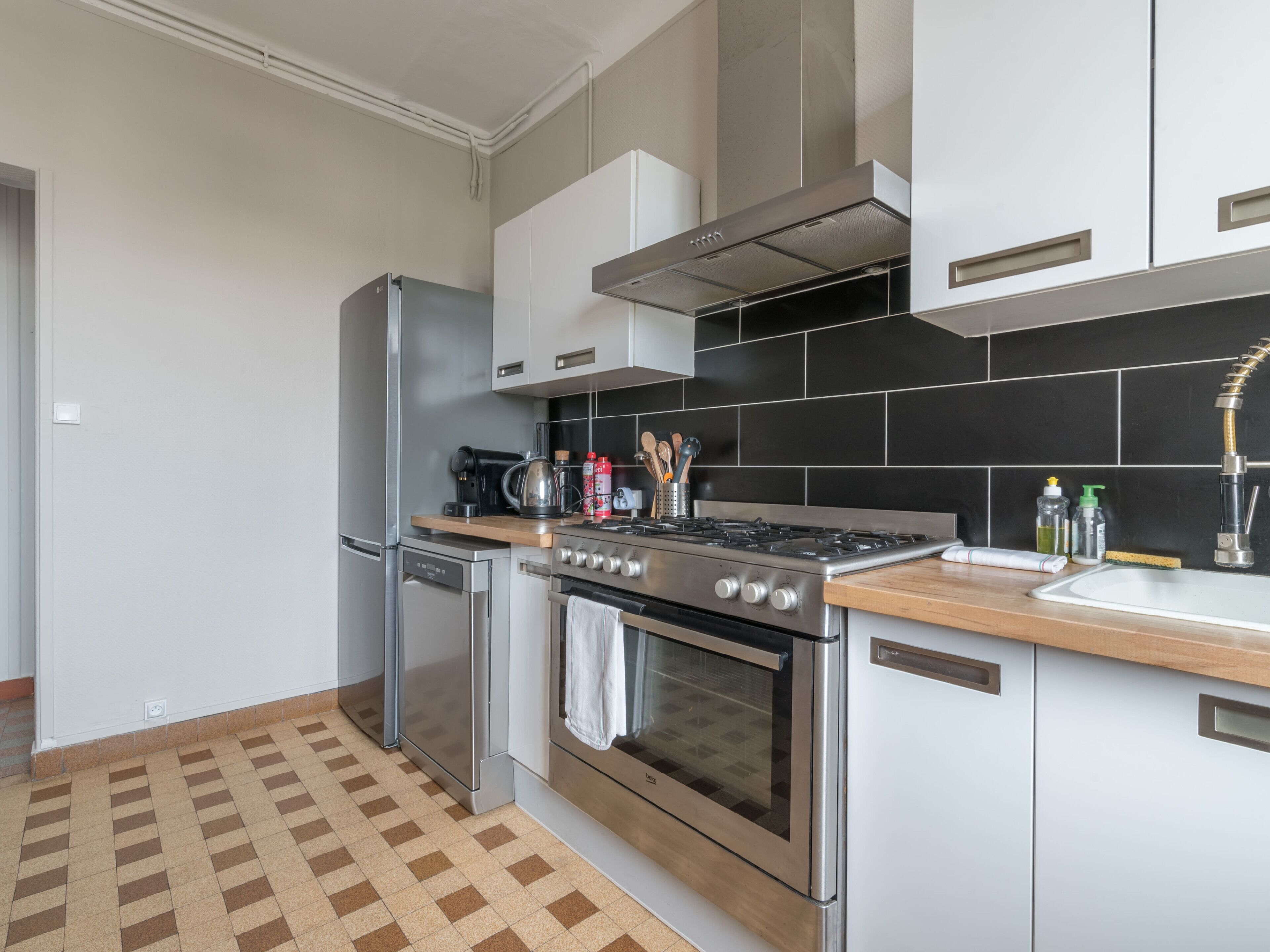 A modern kitchen with stainless steel appliances, a black tiled backsplash, and a wooden countertop.