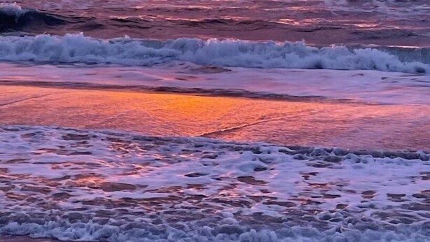 Een zonsondergang boven de oceaan, met golven die de kust naderen.