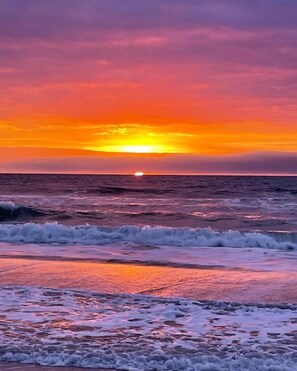 A sunset over the ocean with waves approaching the shore.