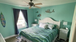 Een slaapkamer met een bed, nachtkastjes, een plafondventilator en vloerkleden met sterrenvisjes.