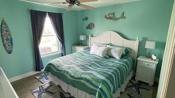 A bedroom with a bed, nightstands, a ceiling fan, and starfish-patterned rugs.