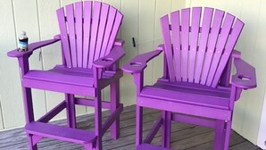 Twee paarse Adirondack stoelen op een houten terras.