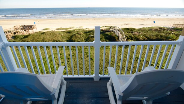 A deck with white railings and two white chairs facing a beach. - Beachfront condo w Sunrise and Sunset Views (Surfside Beach)