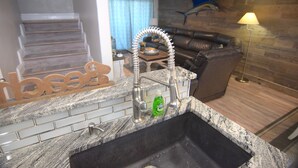 A kitchen with a granite countertop, a stainless steel sink, and a soap dispenser. - Beachfront condo w Sunrise and Sunset Views (Surfside Beach)