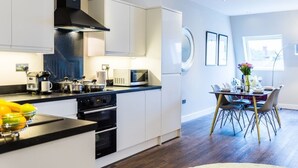 Et moderne køkken med hvide skabe, et sort emfang og et spiseområde med et bord dækket til fire personer.