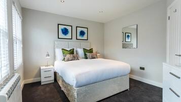 A bedroom with a large bed, a nightstand, a dresser, and a window with blinds.