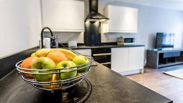 A modern kitchen with a black countertop, a fruit bowl with apples and oranges, white cabinets, and a black range hood.