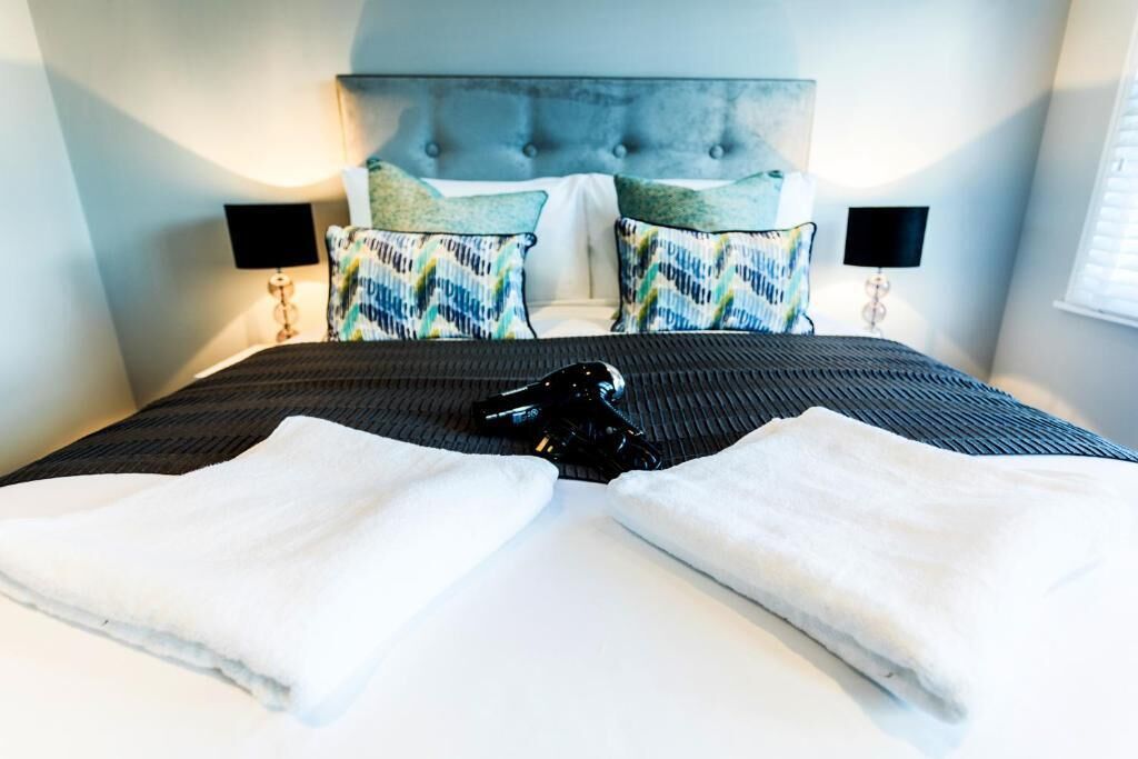 A neatly made bed with a grey headboard, two bedside lamps, and patterned pillows.