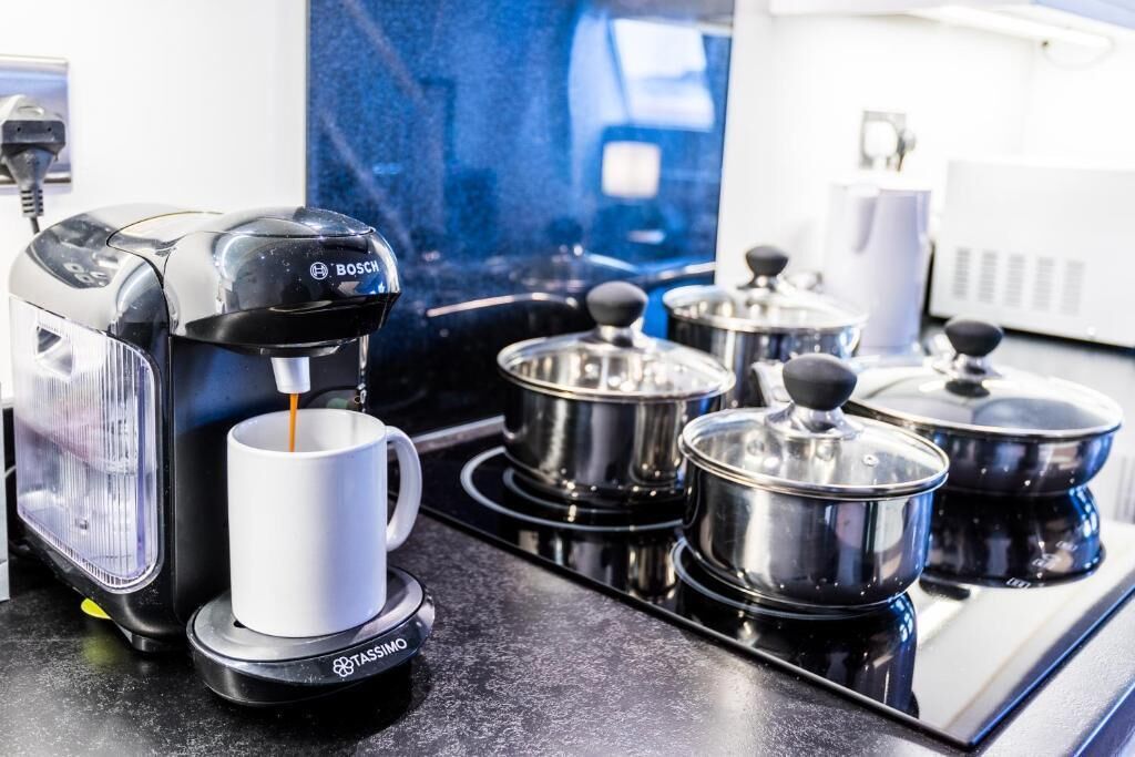 A coffee machine with a cup of coffee, a kettle, and pots on a kitchen counter.
