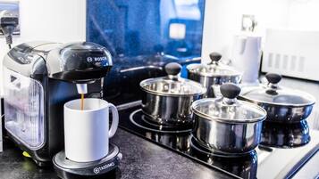 A coffee machine with a cup of coffee, a kettle, and pots on a kitchen counter.