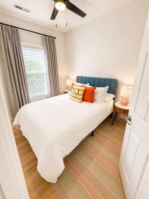A bedroom with a bed, curtains, a ceiling fan, a nightstand, and a lamp.