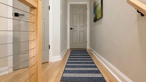 Un pasillo con una escalera de madera, un tapete a rayas blancas y negras y un cuadro en la pared.