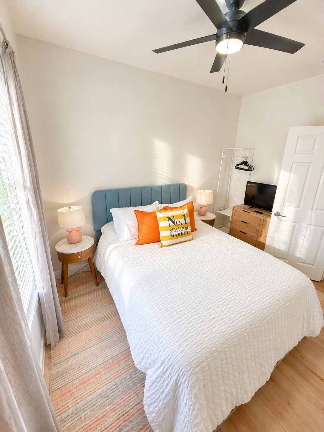A hotel room with a bed, a ceiling fan, a TV, a wardrobe, and a window with curtains.