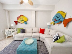 A living room with a beige sectional sofa, a blue ottoman, and two wall-mounted fish decorations.