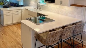 Una cocina moderna con armarios blancos, una isla con taburetes y un microondas, además de una lámpara colgante.