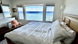 A bedroom with a large bed, a ceiling fan, a view of the sea, and a window with a plant. - Stunning lake cottage in the heart of wine country (Traverse City)