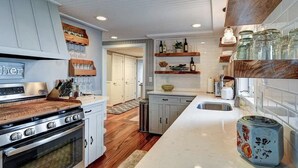 A modern kitchen with wooden countertops, a stainless steel stove, and a built-in oven. There are shelves with glass jars and bottles, and a small island with a sink. - Stunning lake cottage in the heart of wine country (Traverse City)
