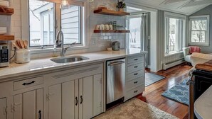 A kitchen with white cabinets, a stainless steel dishwasher, and wooden shelves. - Stunning lake cottage in the heart of wine country (Traverse City)
