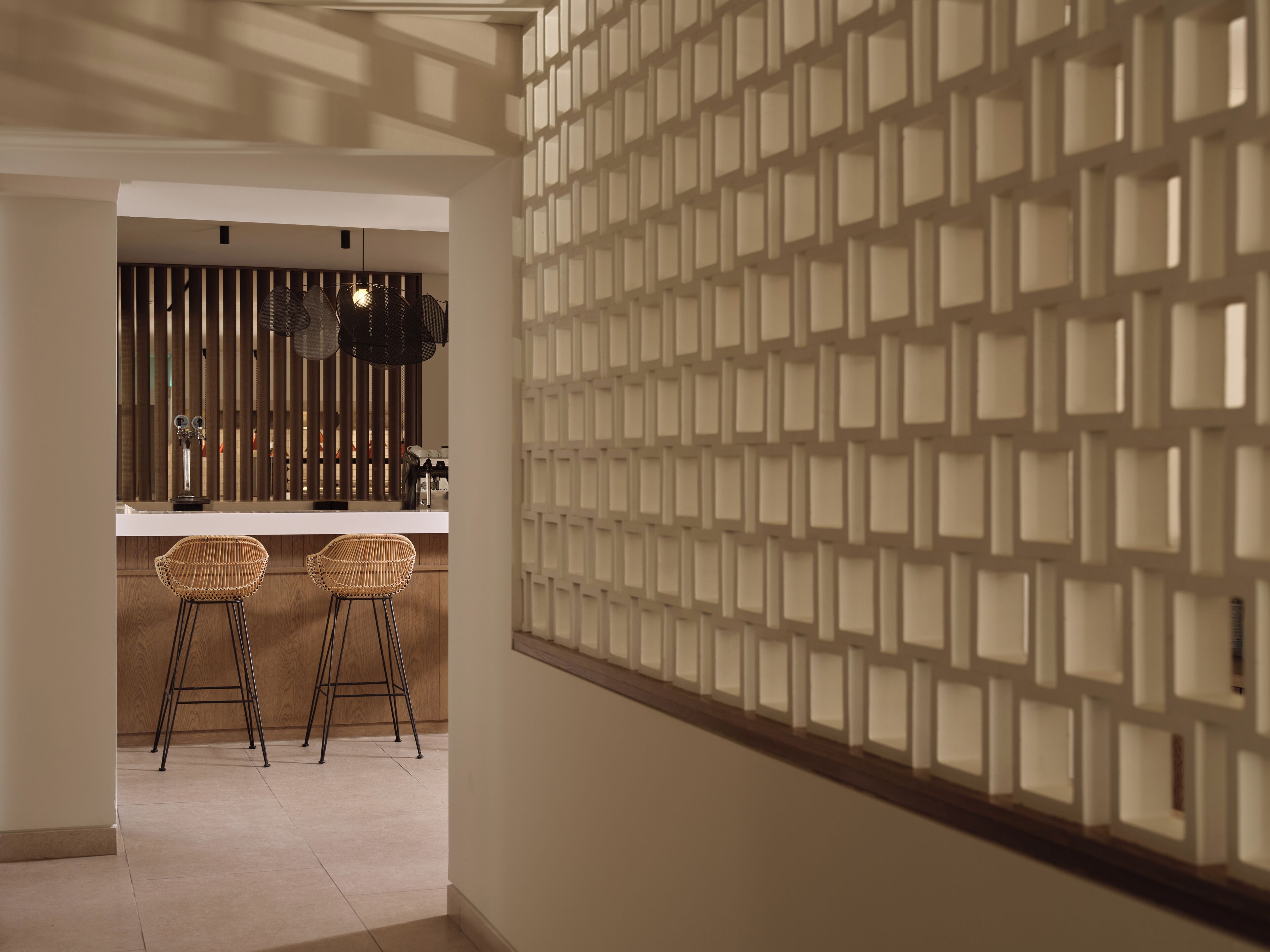 A modern kitchen with a white countertop, two wicker bar stools, and a decorative wall panel.