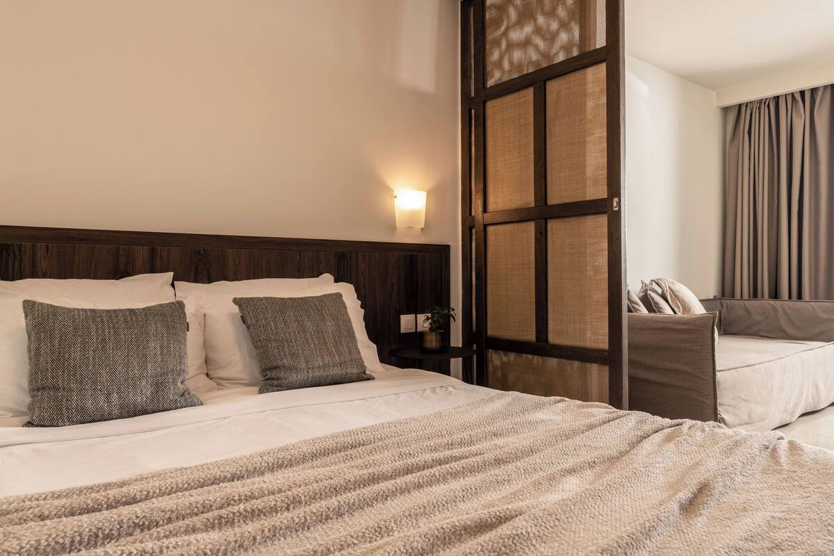 Habitación de hotel con cama, mesita de noche, lámpara de pared y vistas a través de una ventana con cortinas.