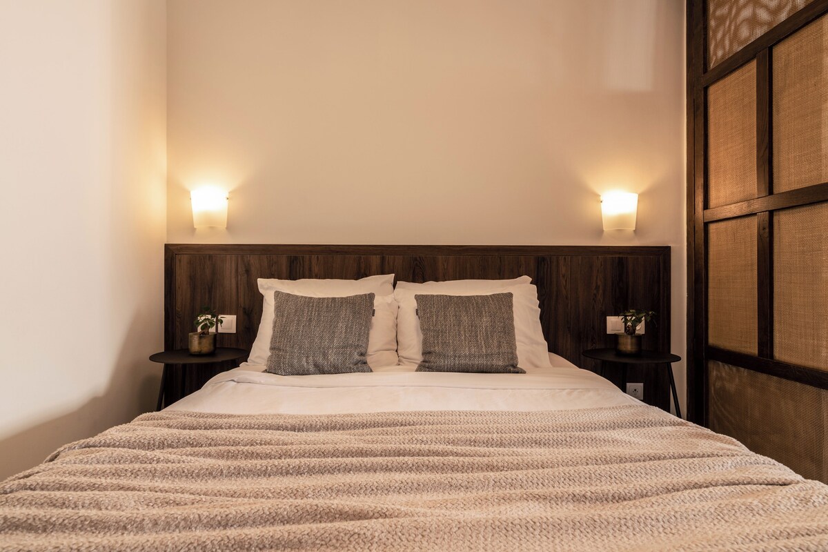 Una cama bien hecha con un edredón a rayas, dos mesitas de noche con lámparas y un cabecero de madera.